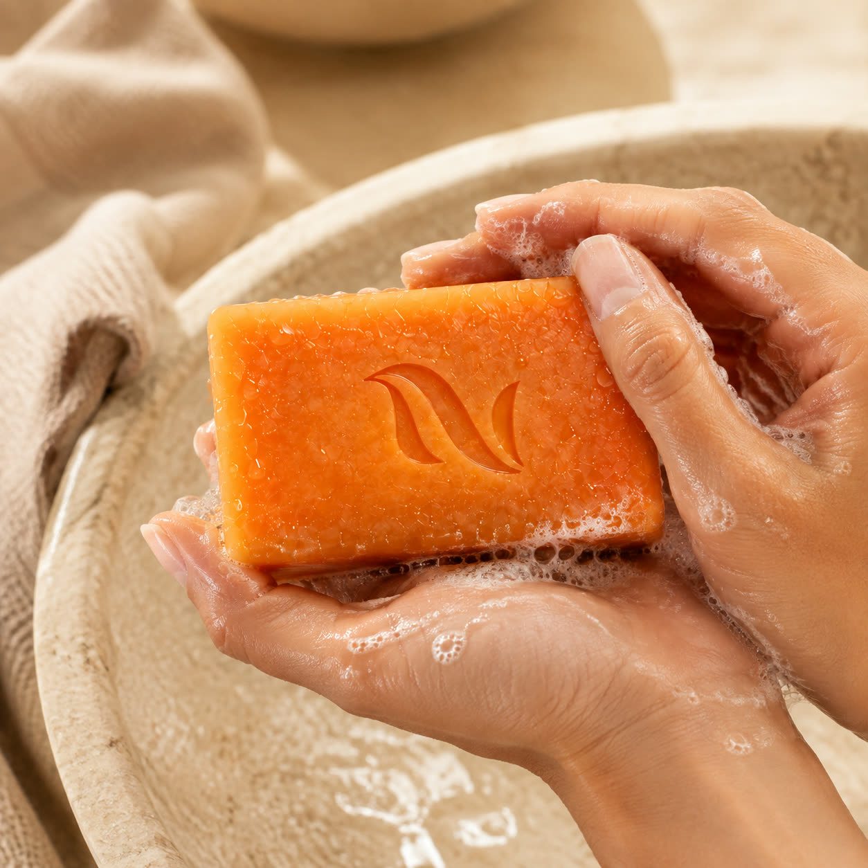 Hands working the NENALI Reset Bar into a lather over a stone bowl